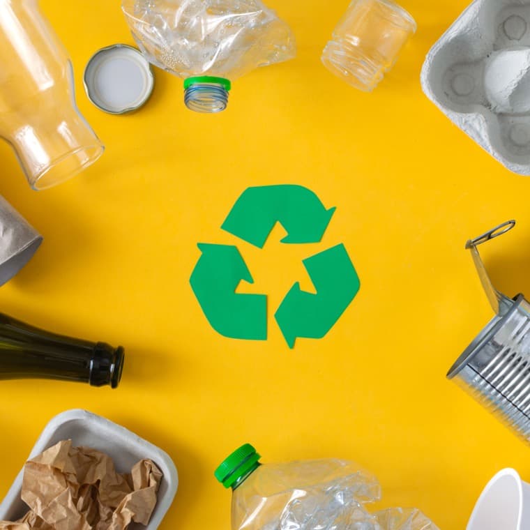 Tomma förpackningar mot en orange bakgrund med en grön återvinningssymbol i mitten.