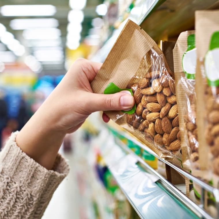 En hand tar ner en förpackning från en hylla i en matbutik.
